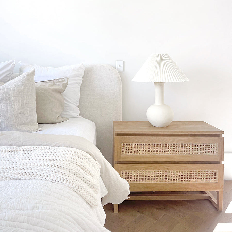 Beach House Wide oak and rattan bedside table styled beside a bed in a coastal bedroom