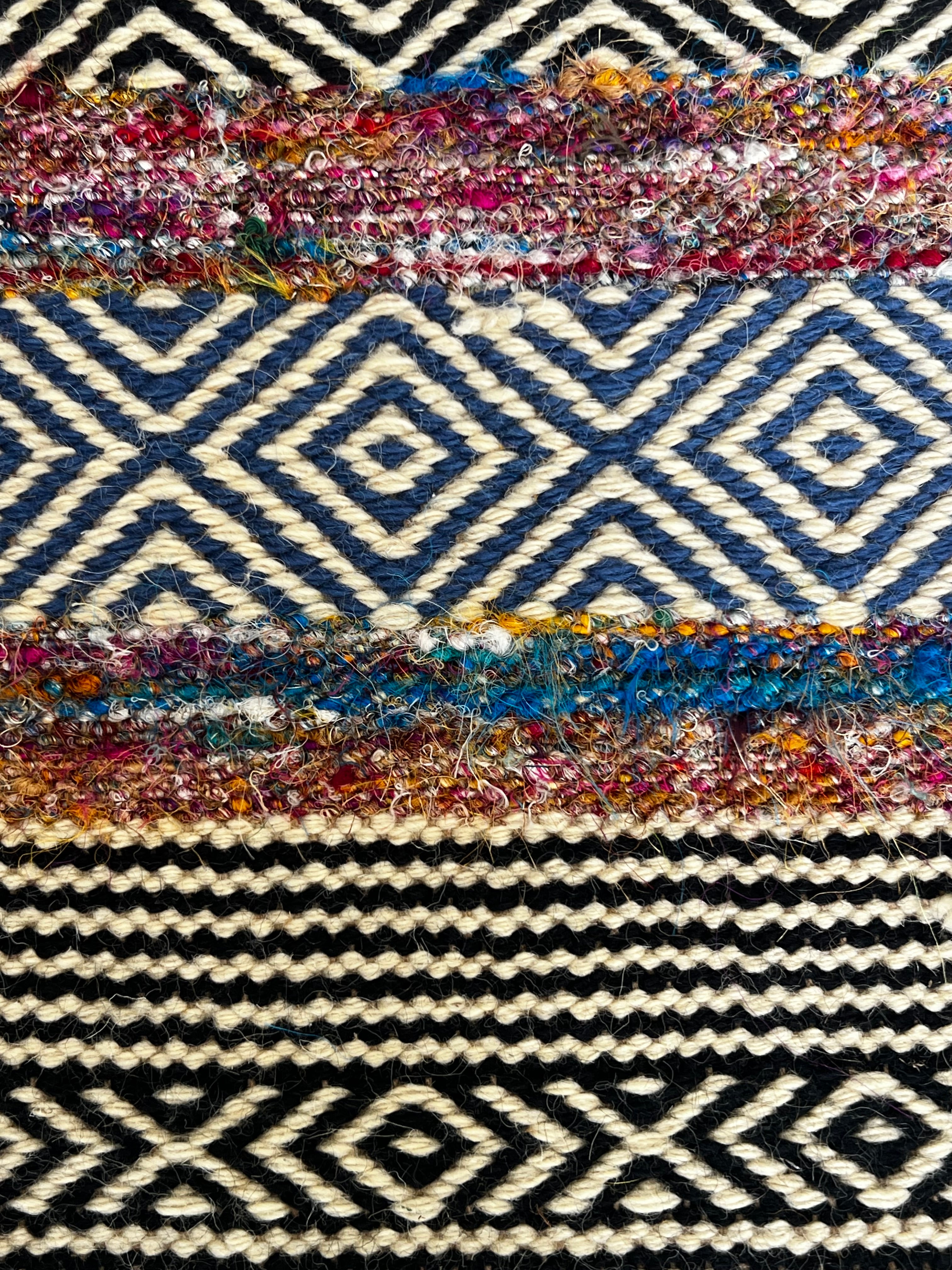Bold patterned rug with natural, black, and blue tones plus pops of color, inspired by global cultures, adding style and character to any room. Close up 2.