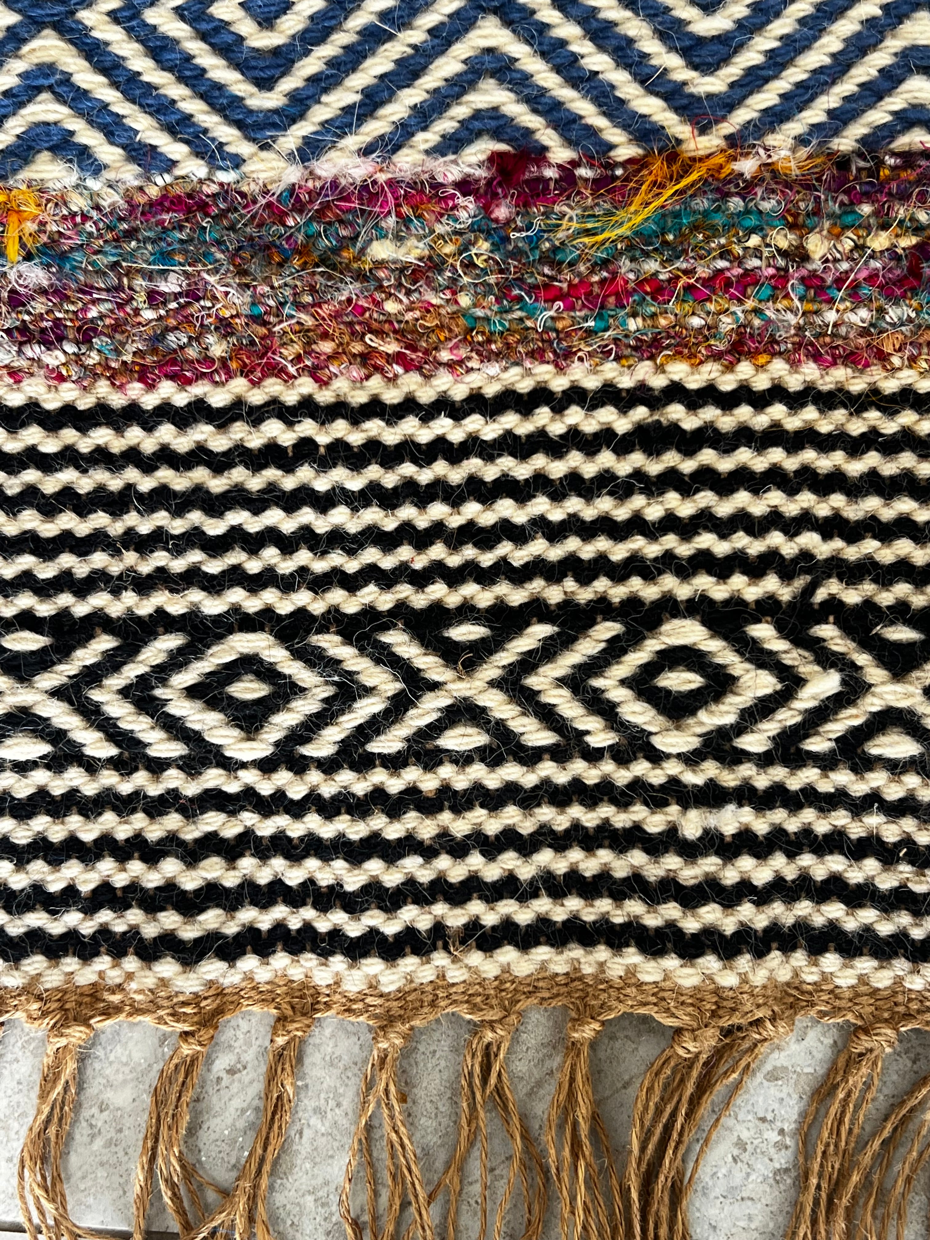 Bold patterned rug with natural, black, and blue tones plus pops of color, inspired by global cultures, adding style and character to any room. Close up.