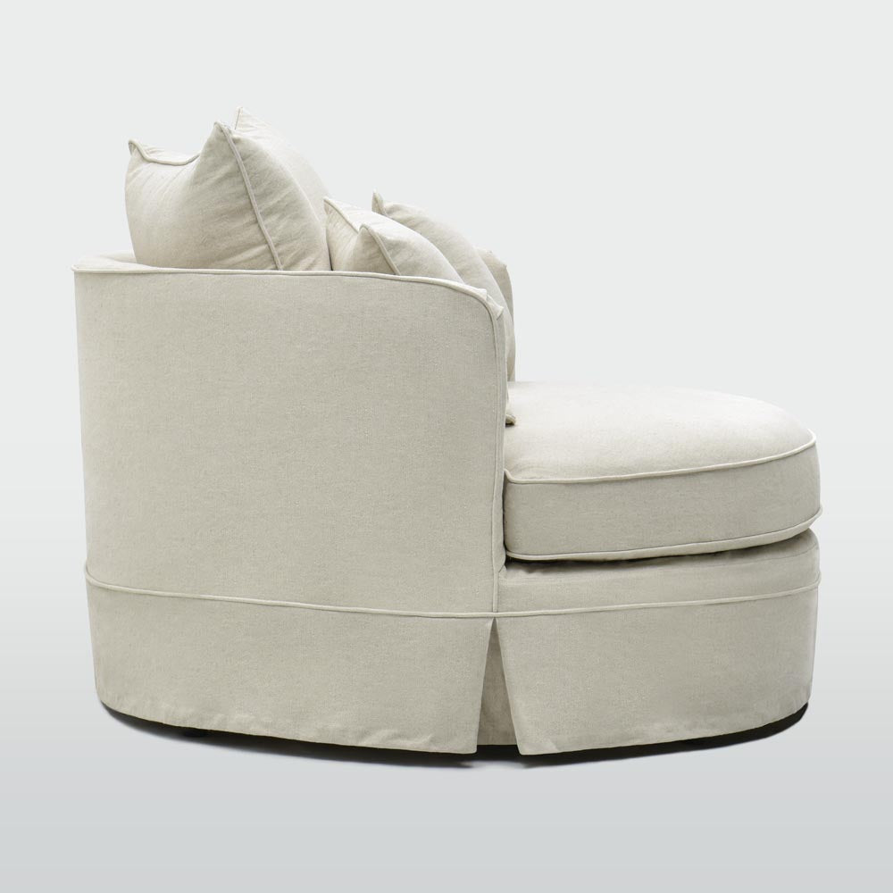 Side view of the Noosa beige snuggle chair showing the curved upholstered back and skirted base