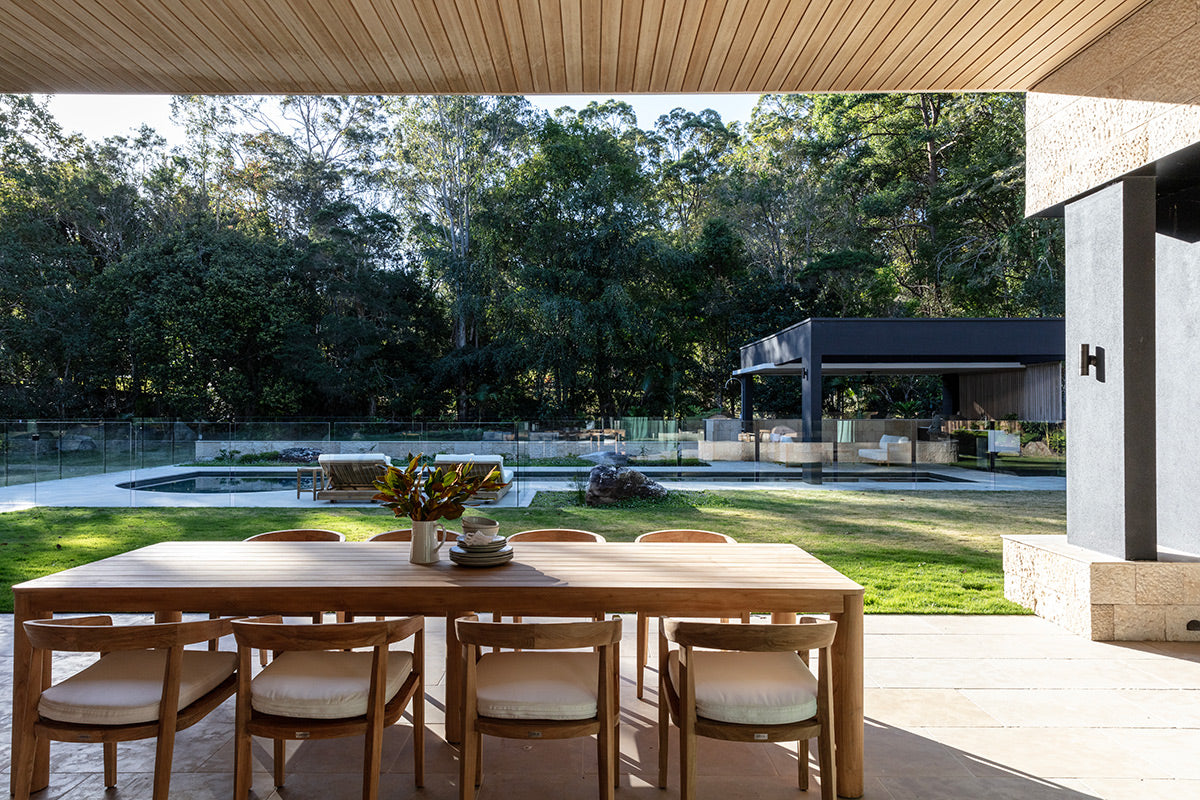 Noosa teak outdoor dining table with timber chairs overlooking a pool and garden