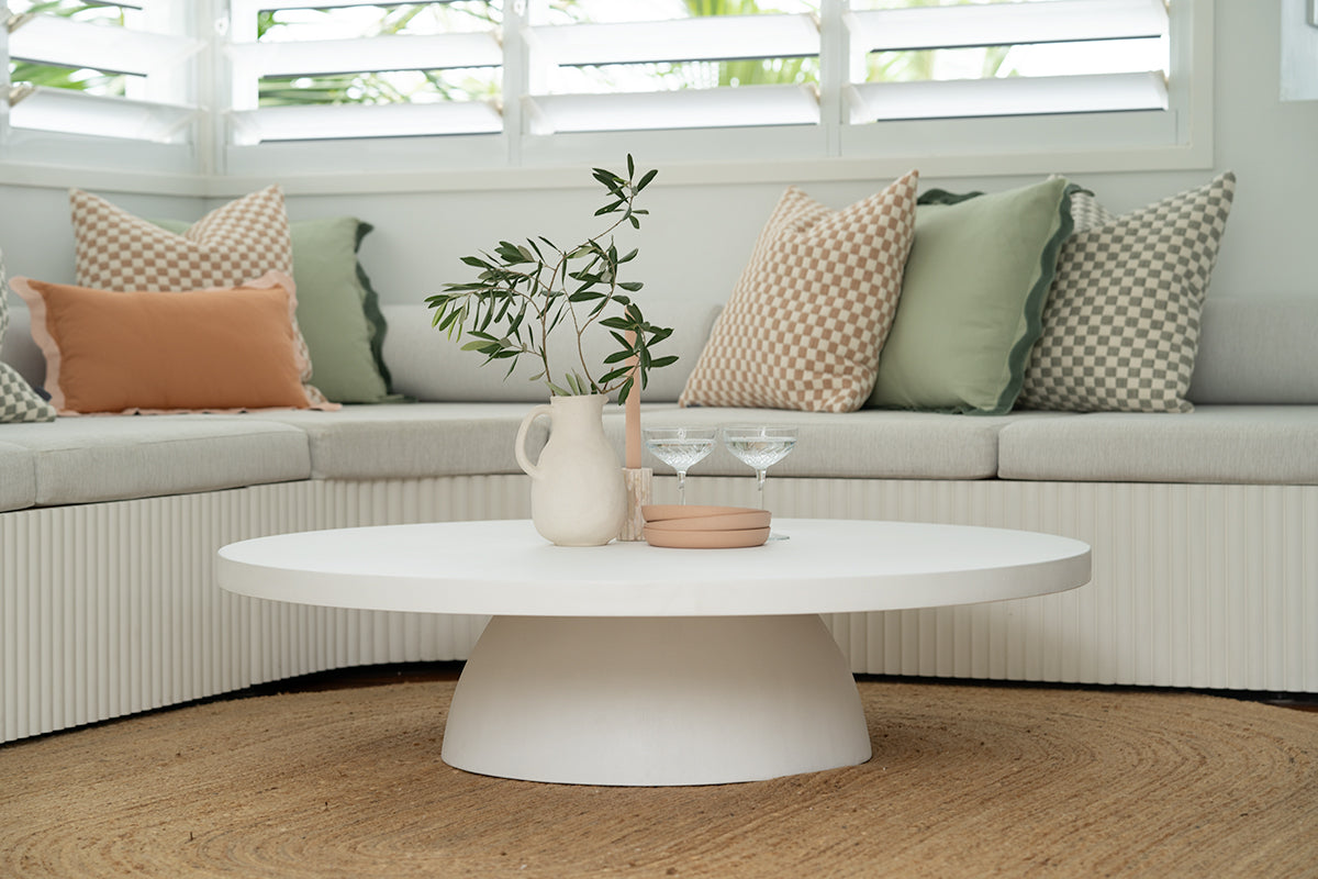 Round white microcement coffee table styled with ceramics and decorative accessories.