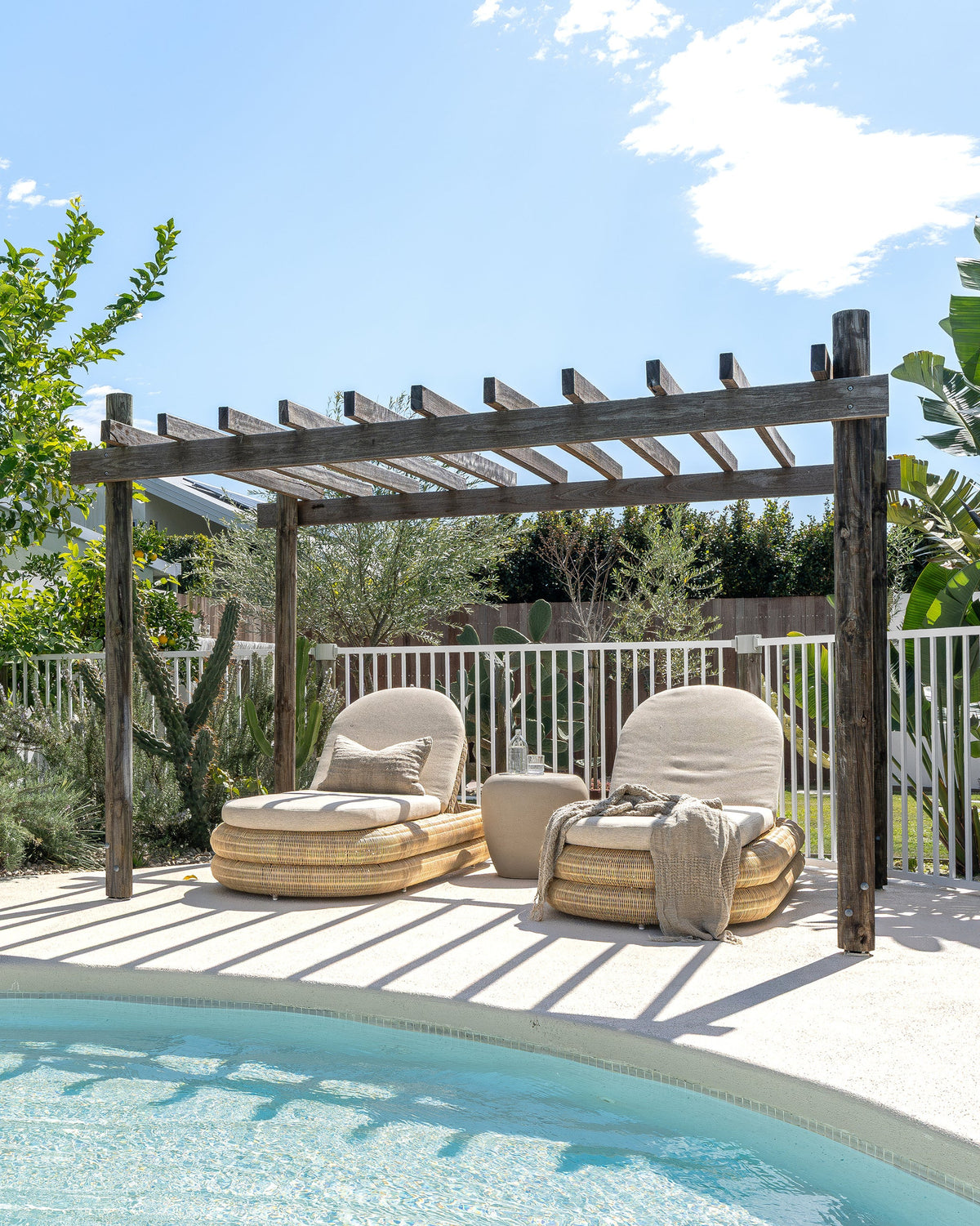 Two Satori outdoor sun loungers with a side table beside a swimming pool under a pergola