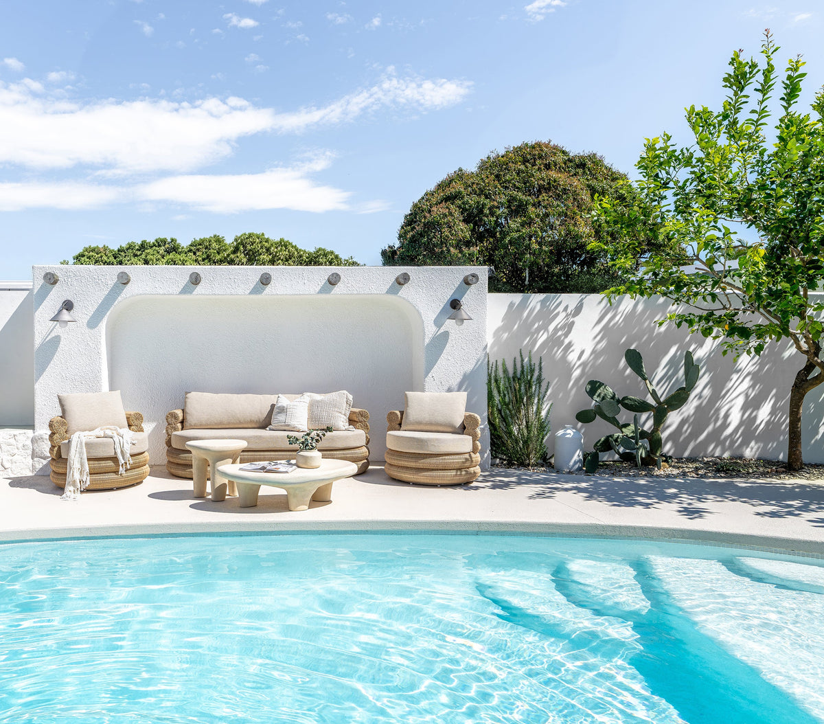 Satori outdoor swivel chairs and sofa styled with sculptural tables beside a swimming pool