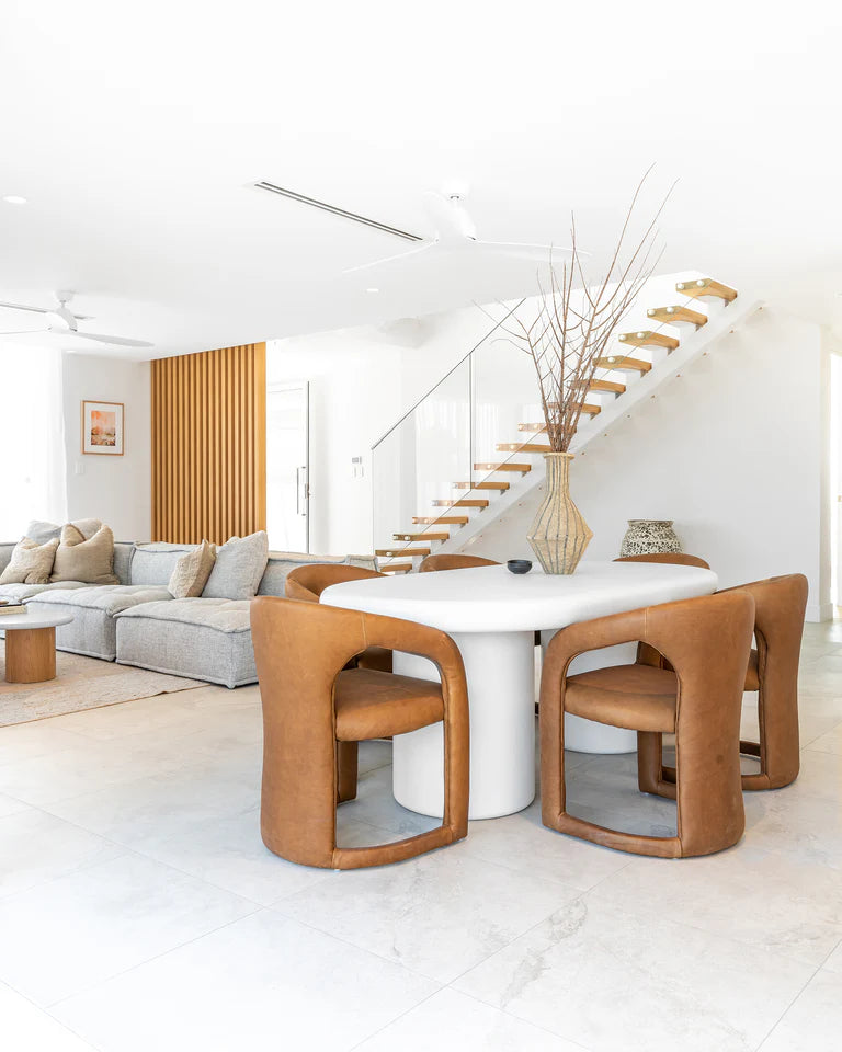 Fikile Dining Chair – contemporary chair with swooping open back, upholstered leather seat, and rounded silhouette, blending vintage style with modern elegance for dining or accent use. Styled beautifully in this dining space.