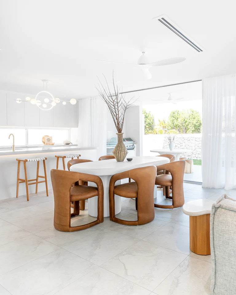 Fikile Dining Chair – contemporary chair with swooping open back, upholstered leather seat, and rounded silhouette, blending vintage style with modern elegance for dining or accent use. Styled beautifully in this modern dining room.