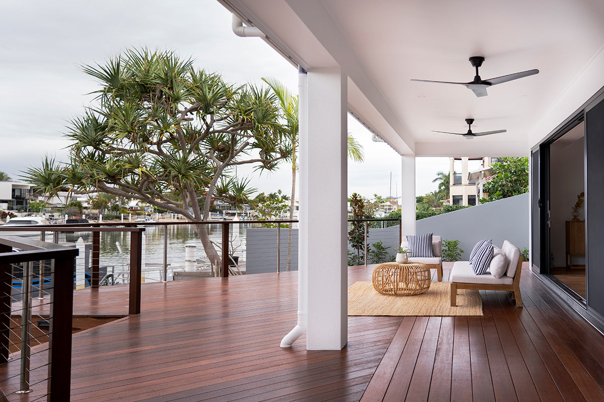 Bedarra teak outdoor three-seater sofa, covered verandah setting with timber decking, a woven table and coastal planting