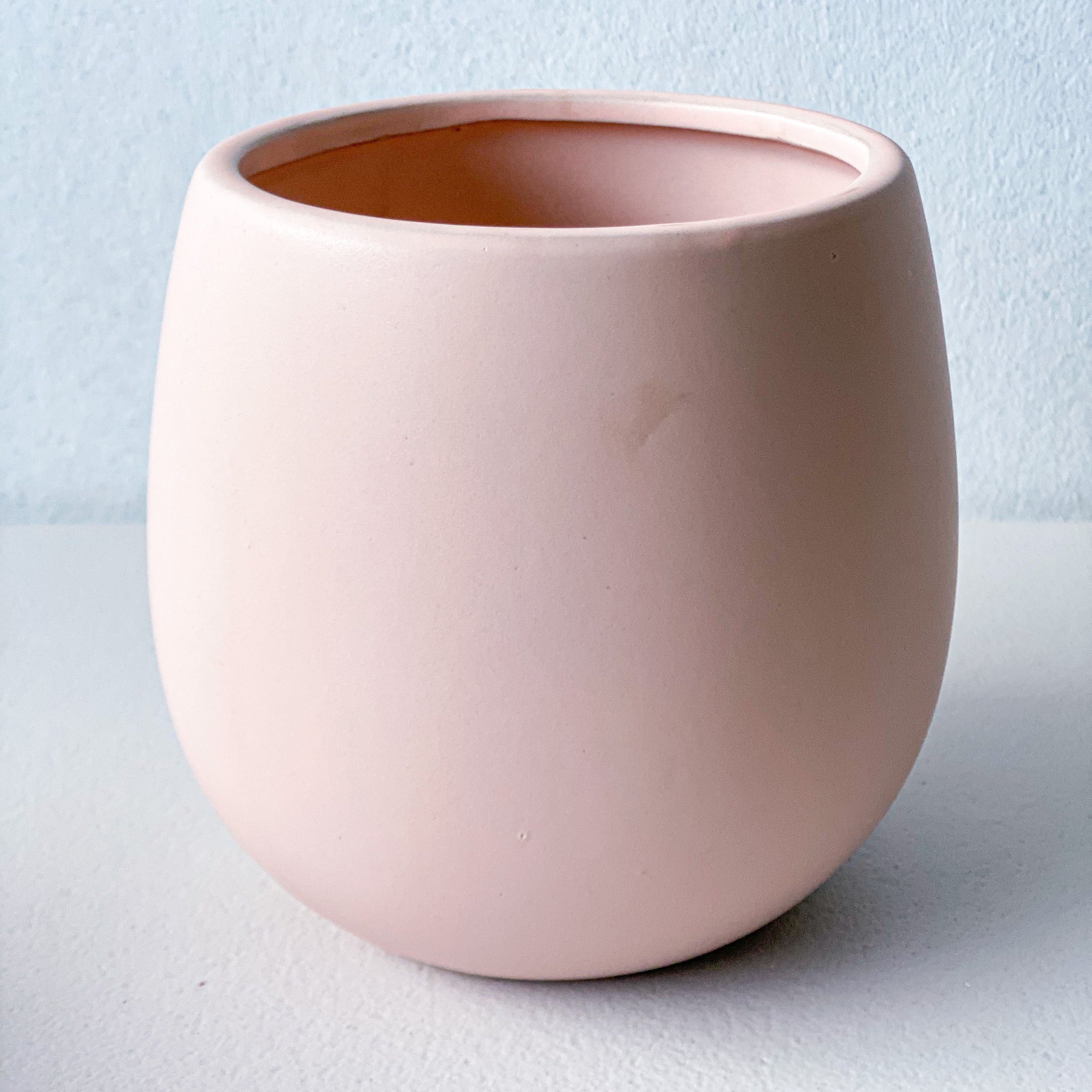 A minimalist, rounded ceramic planter pot in a soft blush pink color, shown from a three-quarter angle on a solid white background.