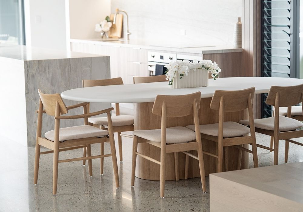 Modern coastal dining space with an oval timber dining table surrounded by upholstered chairs and light natural décor.