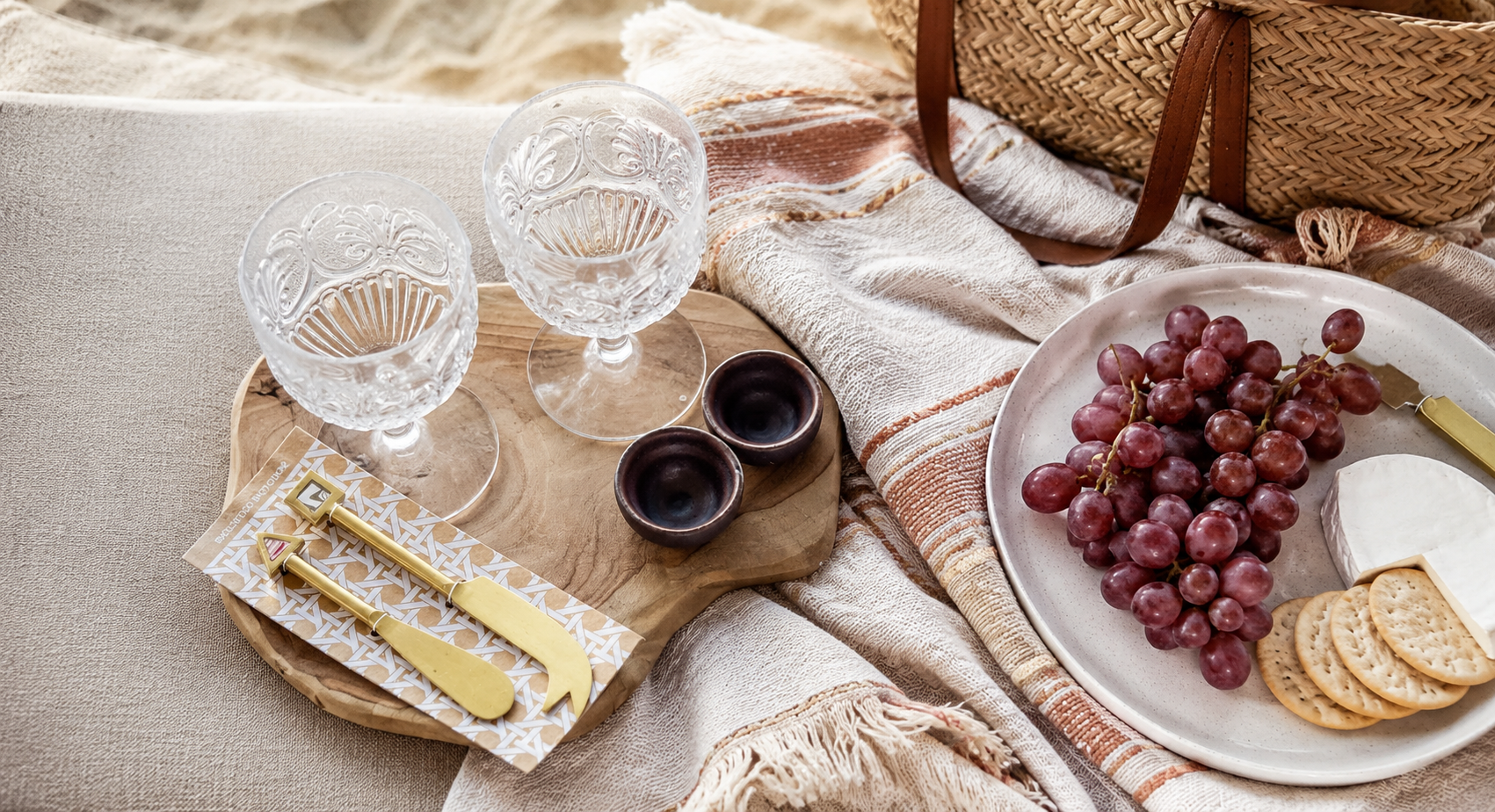 Modern picnic accessories styled on a timber serving board with crystal wine glasses, cheese knives, ceramic bowls and a soft woven picnic blanket, perfect for outdoor entertaining in Australia.