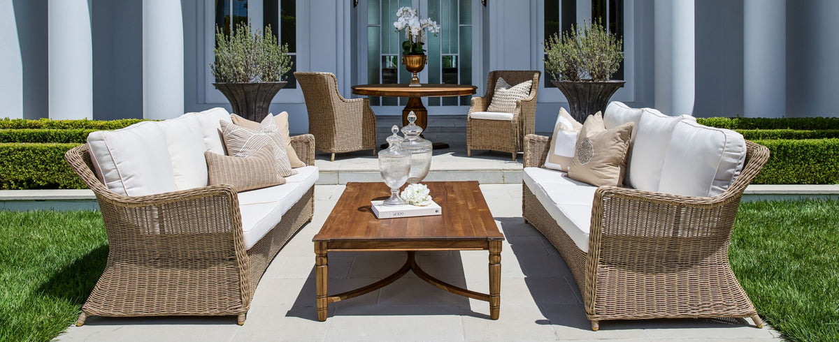 Ashford natural woven outdoor sofas and lounge chairs with light cushions arranged around a coffee table on a paved terrace
