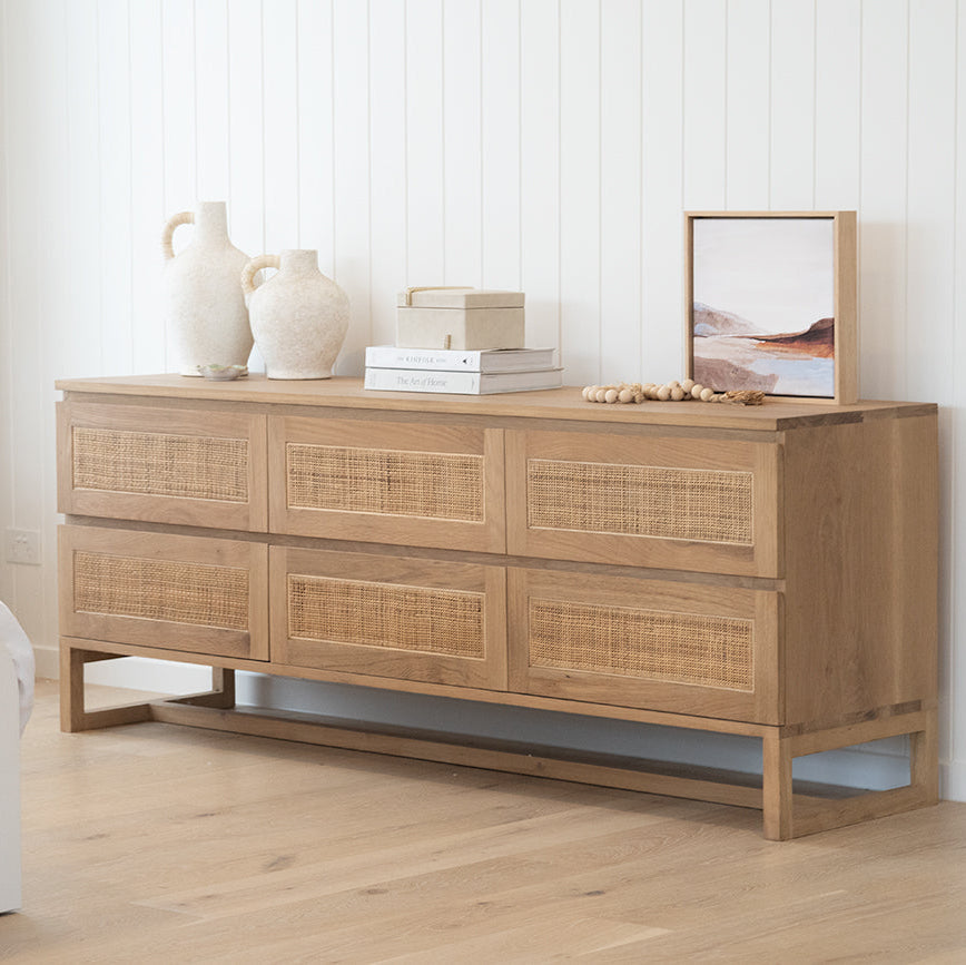 Beach House oak and rattan chest styled beside a bed with ceramics and a framed mirror
