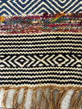 Load image into Gallery viewer, Bold patterned rug with natural, black, and blue tones plus pops of color, inspired by global cultures, adding style and character to any room. Close up.