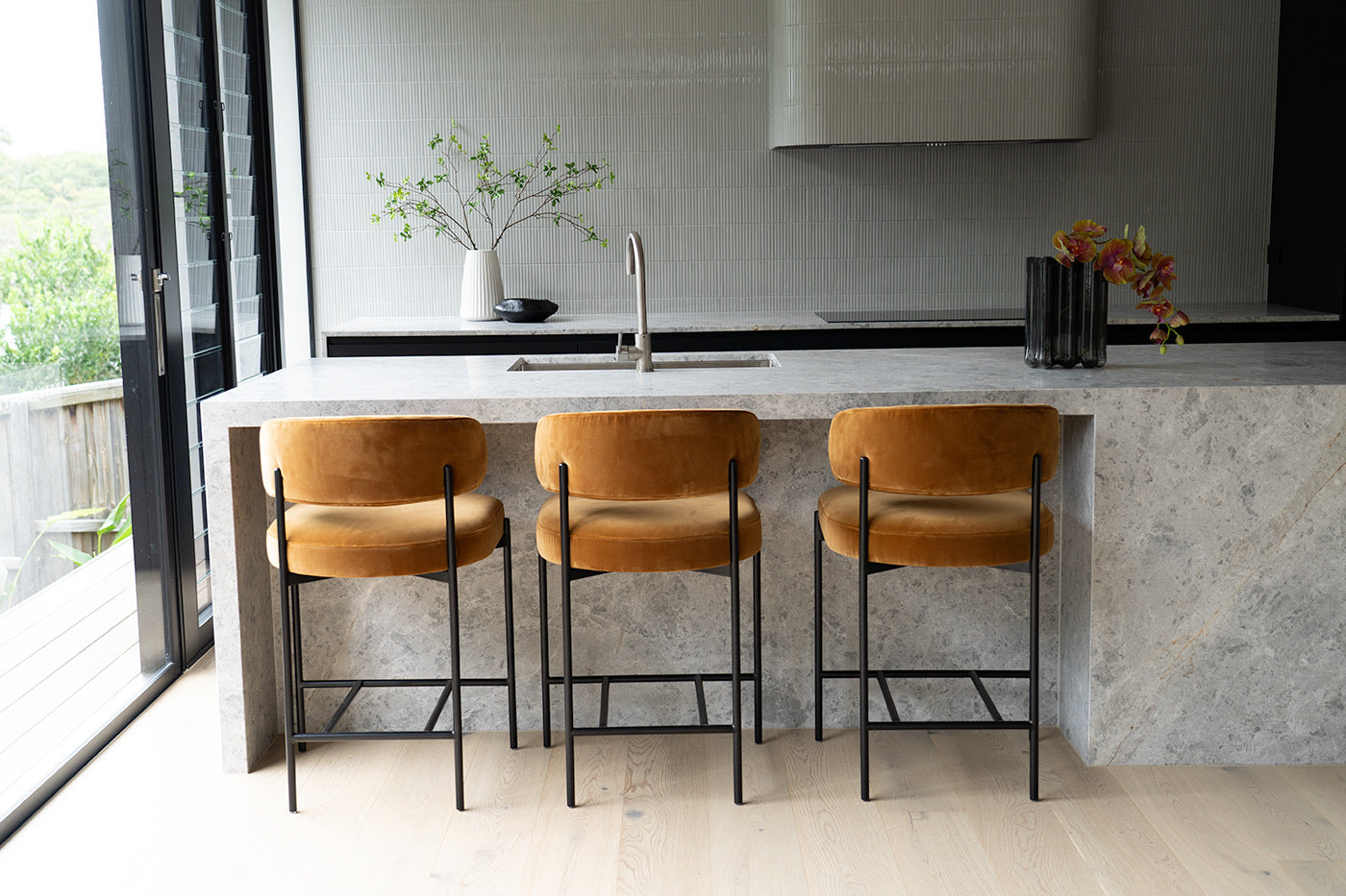 Fontaine Counter Stool with half-moon curved back and metal legs, upholstered in performance velvet in amber, modern Art Deco inspired counter stool for elegant interiors.  Modern kitchen interior.