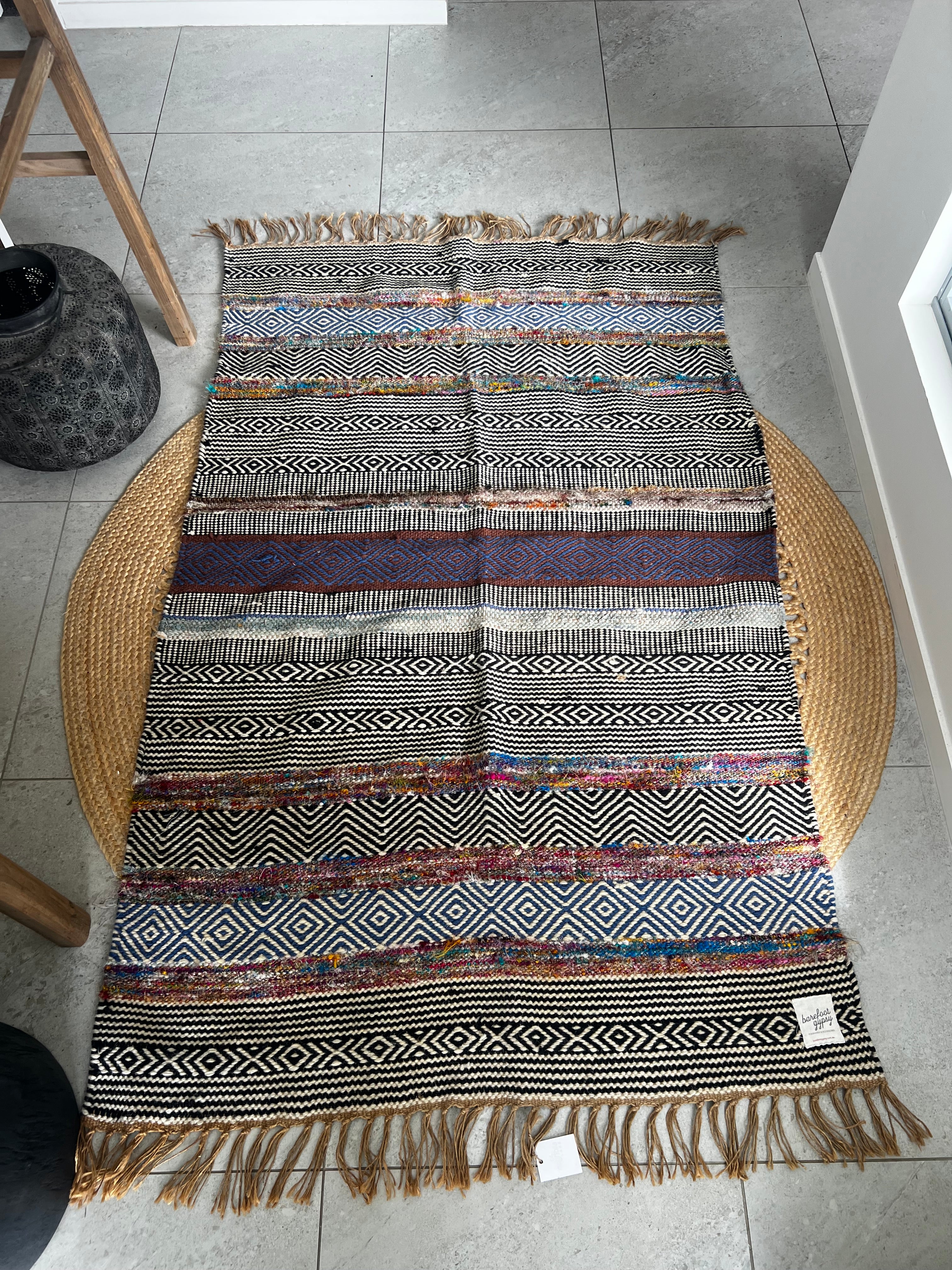 Bold patterned rug with natural, black, and blue tones plus pops of color, inspired by global cultures, adding style and character to any room. Full length perspective.