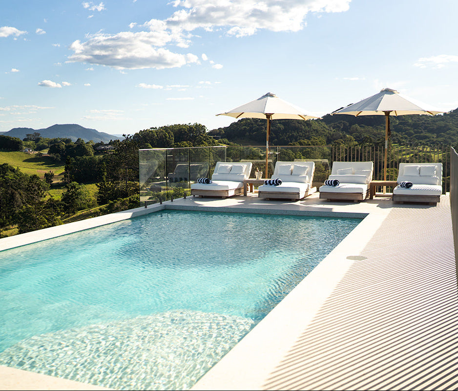 Harbour Island Outdoor Sun Lounger in Grade A teak with white Sunbrella® cushions beside a luxury swimming pool.