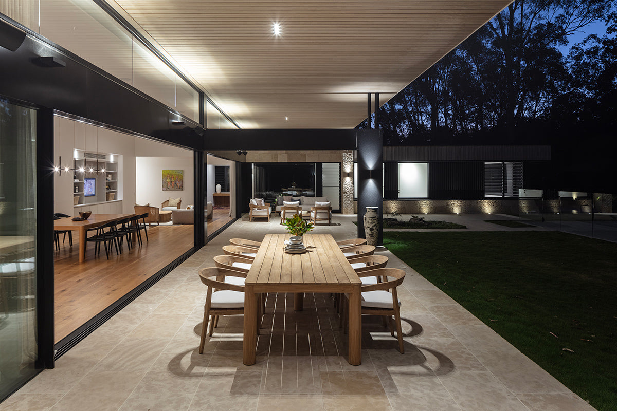 Noosa teak outdoor dining table with timber chairs in a covered outdoor entertaining area at night