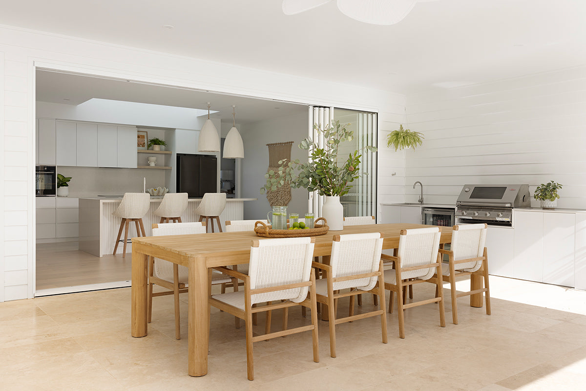 Noosa teak outdoor dining table with white outdoor chairs in a light covered entertaining area
