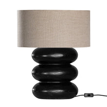 Load image into Gallery viewer, Rundu Table Lamp handcrafted from solid munggur wood with hand-carved textured grooves, showcasing natural wood variations and a soft ambient glow. Black base with oatmeal shade.