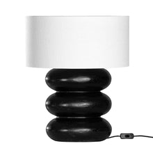 Load image into Gallery viewer, Rundu Table Lamp handcrafted from solid munggur wood with hand-carved textured grooves, showcasing natural wood variations and a soft ambient glow. Black base with white shade.