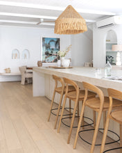 Load image into Gallery viewer, Loki Bar Chair in solid oak with natural finish, featuring sculptural minimalist design, rich wood grain, and black iron footrest for a modern touch. Styled beautifully in this modern kitchen.