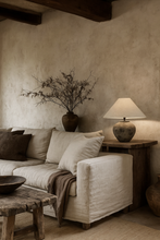 Load image into Gallery viewer, The Villa Table Lamp featuring an organic, rustic design with a natural shade and sculptural base, adding earthy elegance to any space. Wabi Sabi style, Magnolia Lane.  AI impression of how this beautiful lamp could look in a rustic living room with an earthy aesthetic.