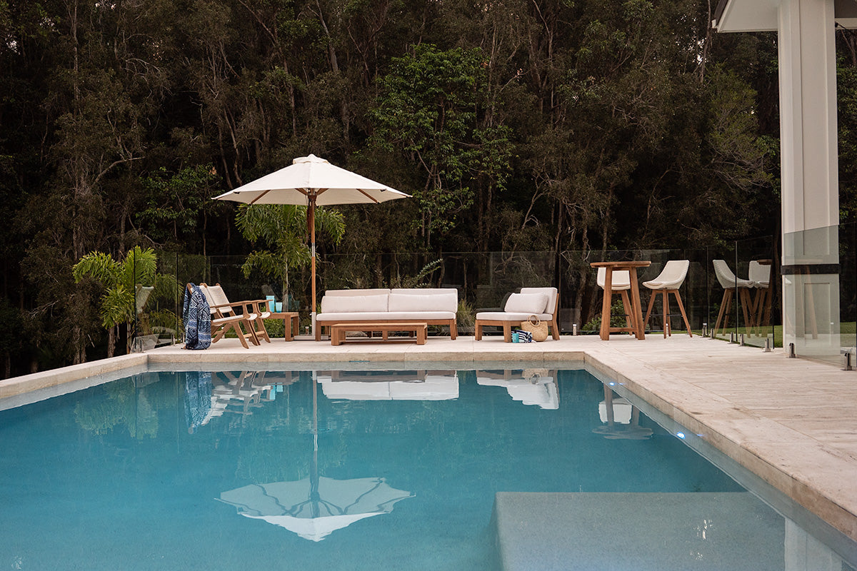 Bedarra teak outdoor three-seater sofa, wide garden and pool setting with the outdoor sofa and coordinating seating