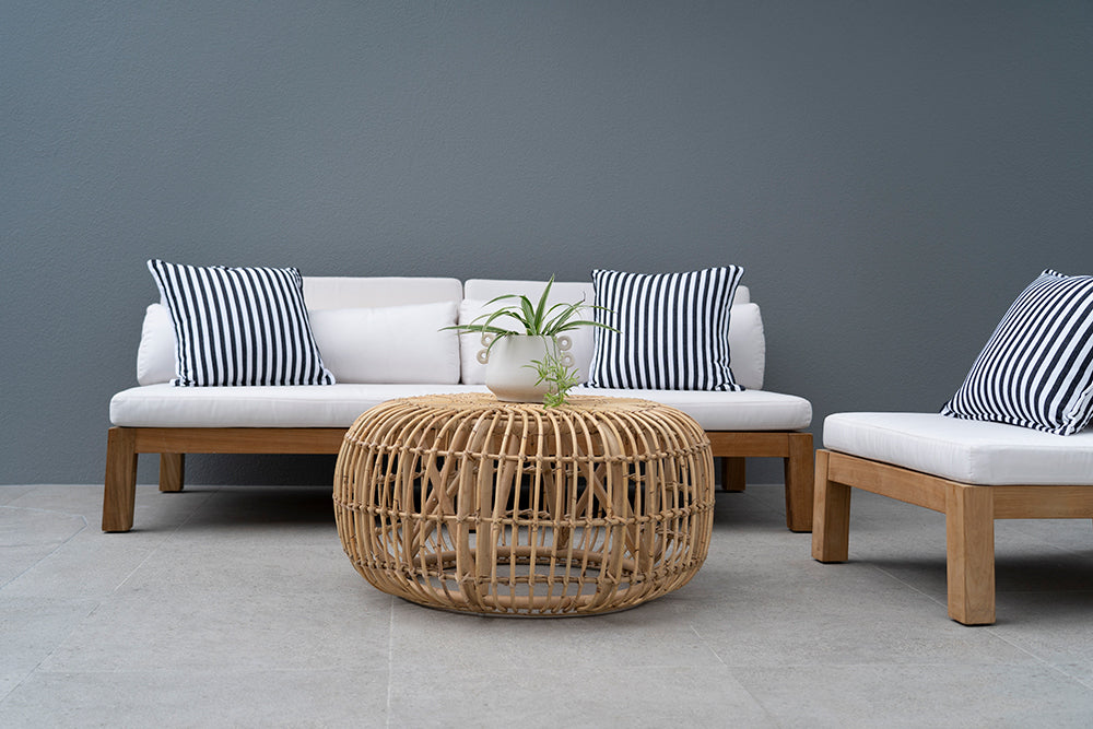 Bedarra teak outdoor three-seater sofa, styled sofa and matching chair with striped cushions and a woven coffee table against a blue wall