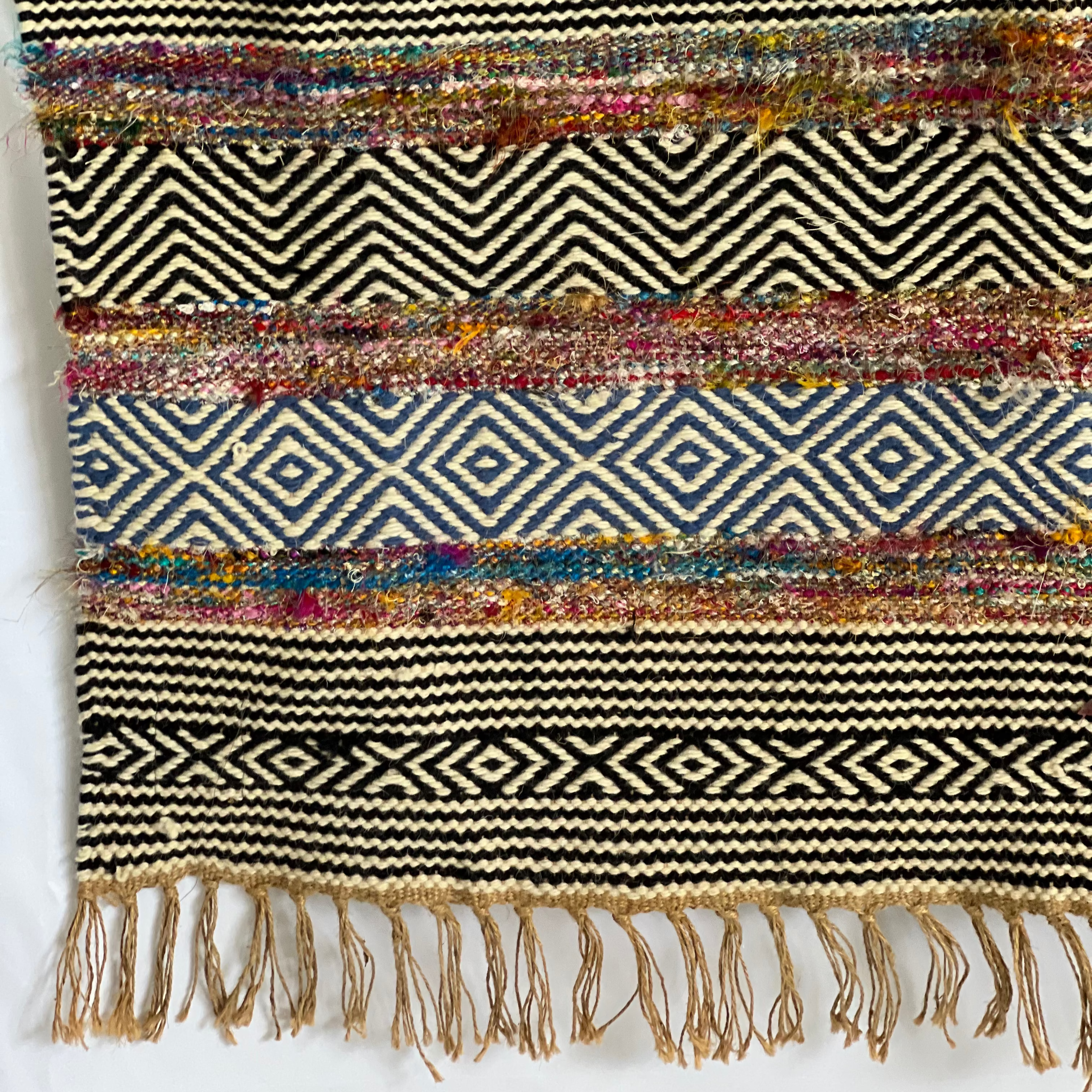 Bold patterned rug with natural, black, and blue tones plus pops of color, inspired by global cultures, adding style and character to any room.