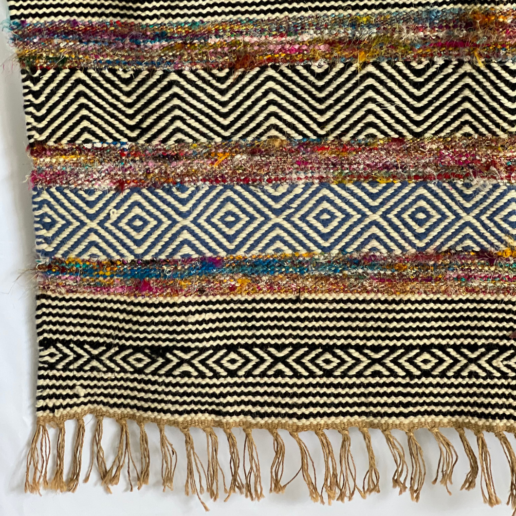 Bold patterned rug with natural, black, and blue tones plus pops of color, inspired by global cultures, adding style and character to any room.